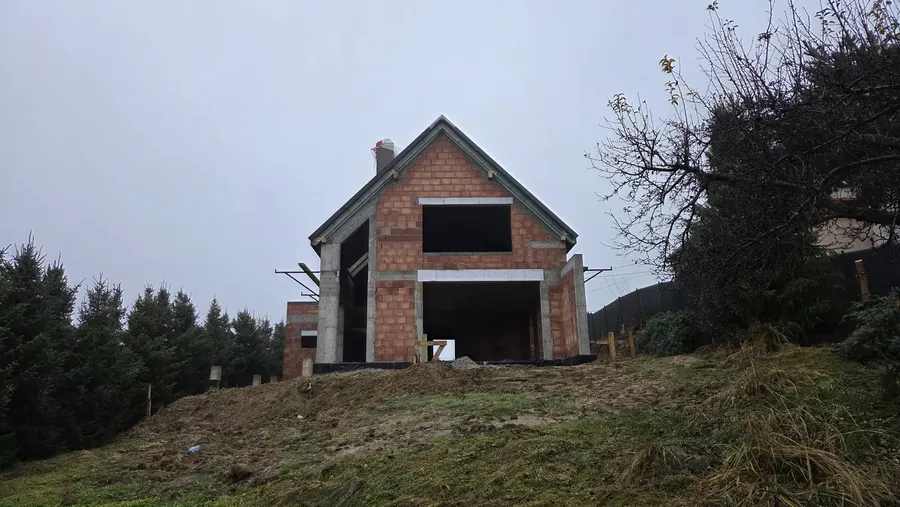 Dom w stanie surowym na szczycie skarpy, widok od doliny